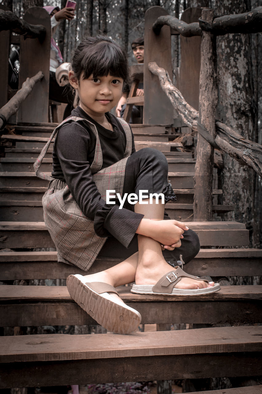 Portrait of girl looking away while sitting on wood