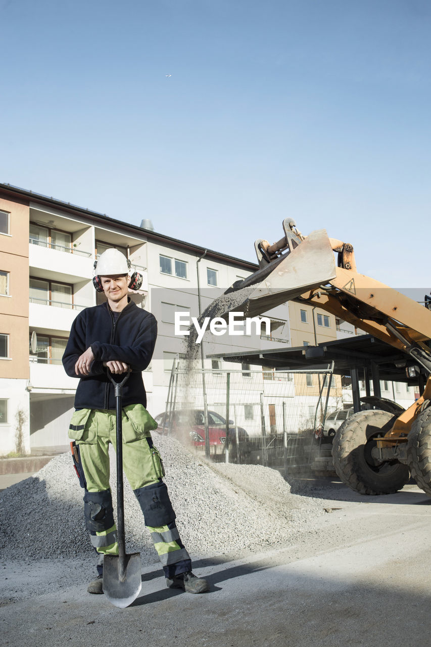 Full length portrait of confident construction worker with shovel standing at site