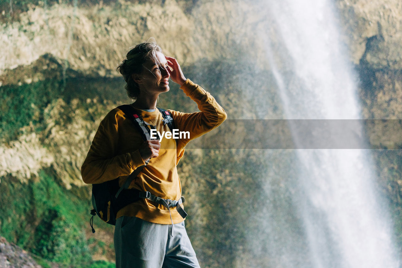 Portrait of an active woman hiker with a backpack in a mountain canyon near a large waterfall.