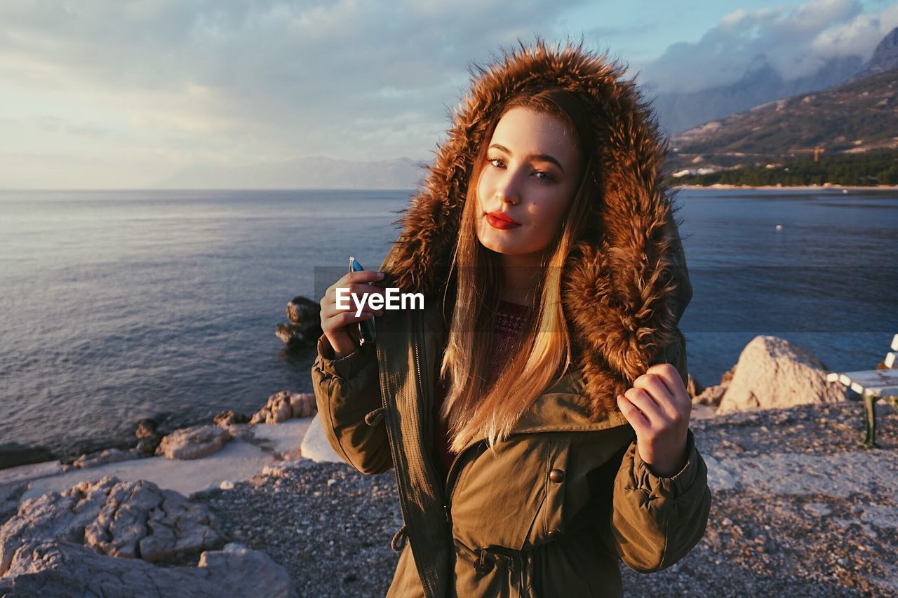 Portrait of beautiful young woman standing by sea against sky