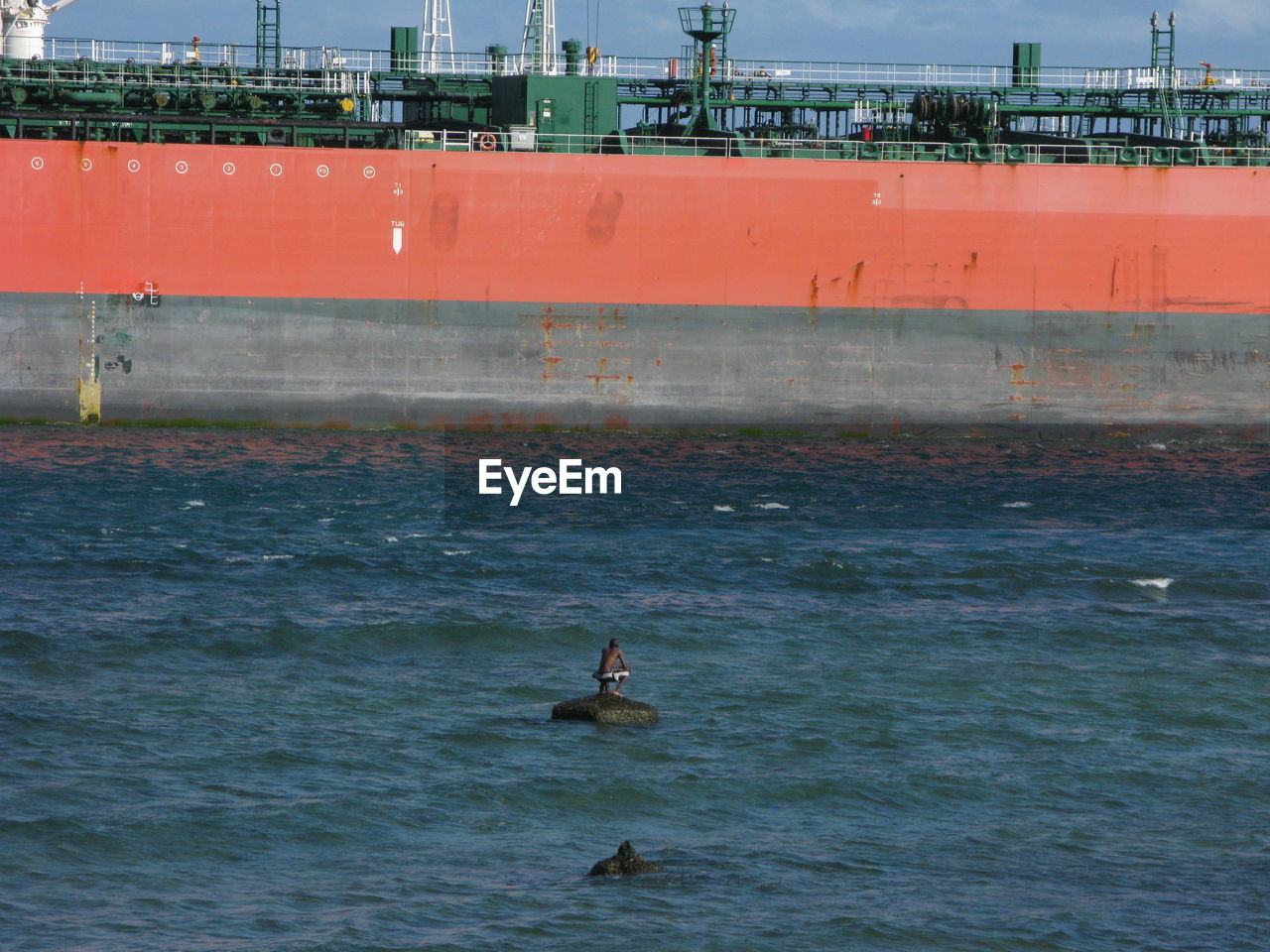 Distance view of man on rock in sea against ship