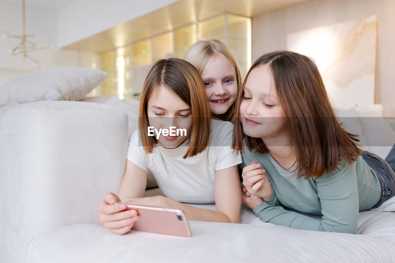 smiling friends using laptop while sitting on bed at home