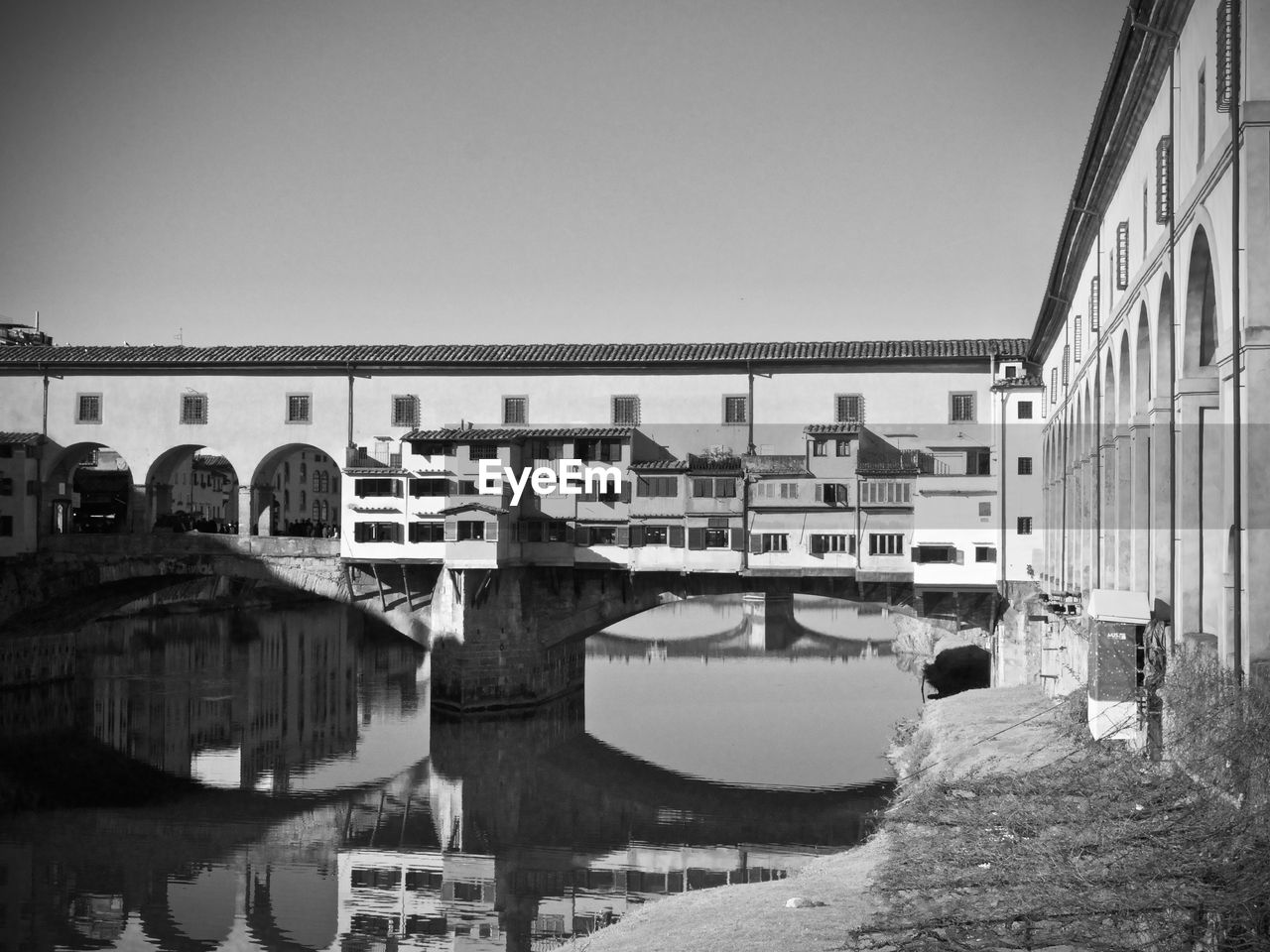 Bridge over river by buildings against clear sky