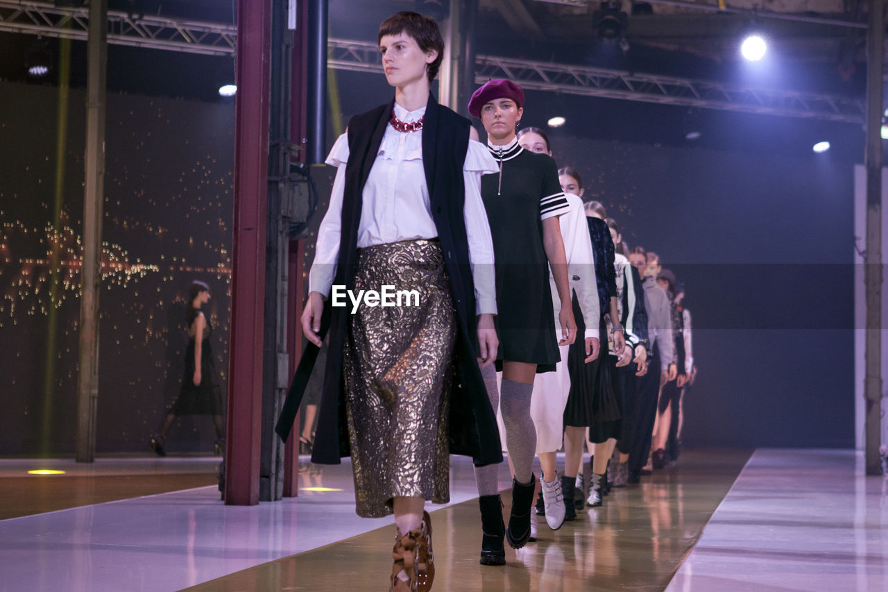 YOUNG WOMEN STANDING IN ILLUMINATED CORRIDOR