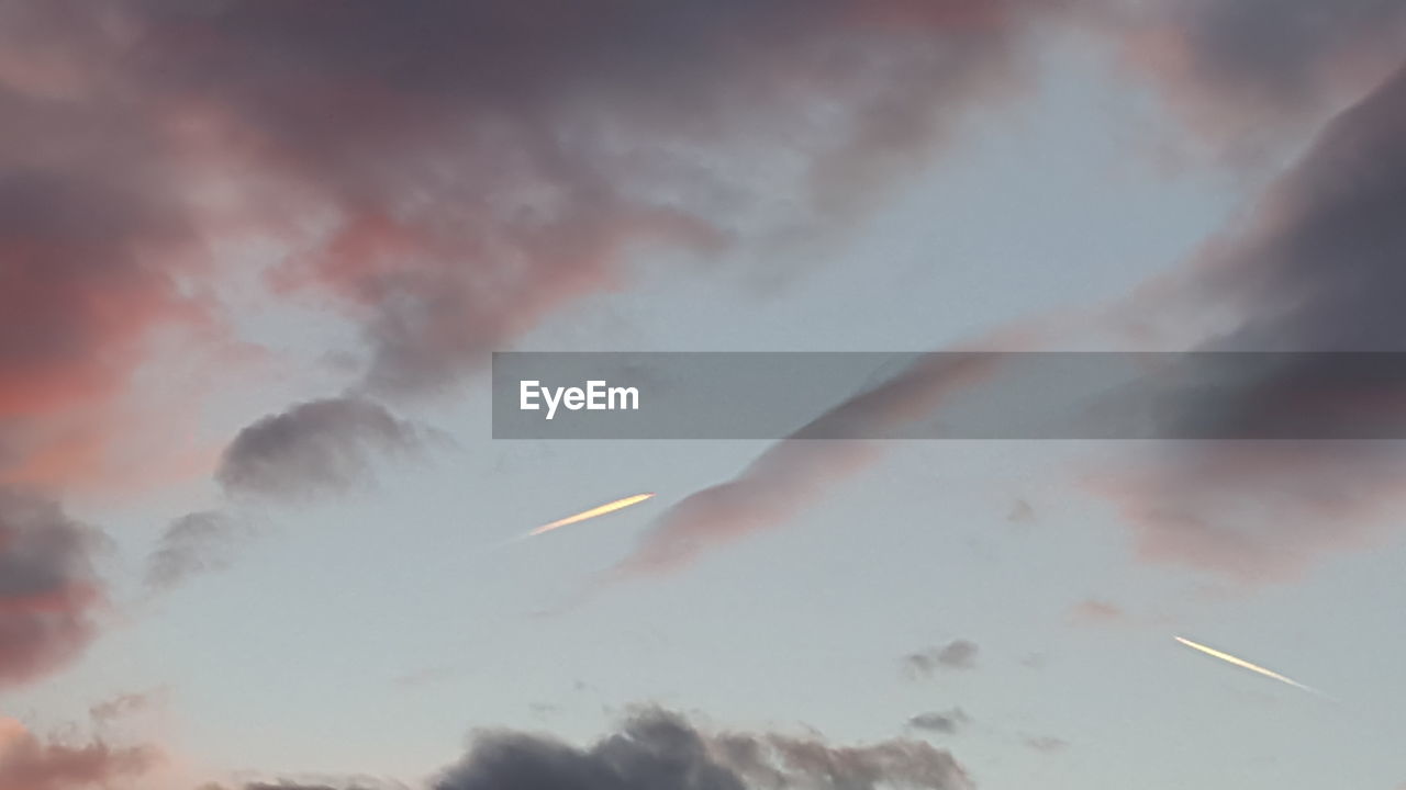 Low angle view of vapor trail in sky at sunset