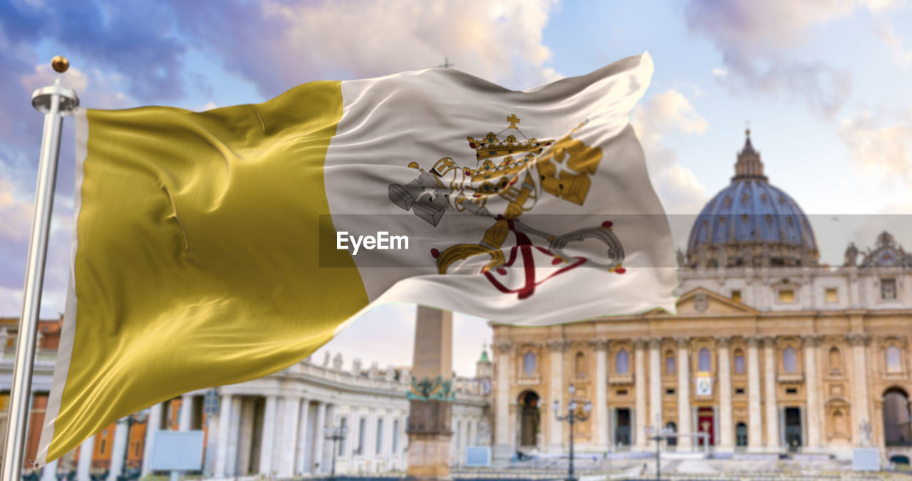 The flag of the vatican city fluttering in the wind with st. peter's basilica in the background