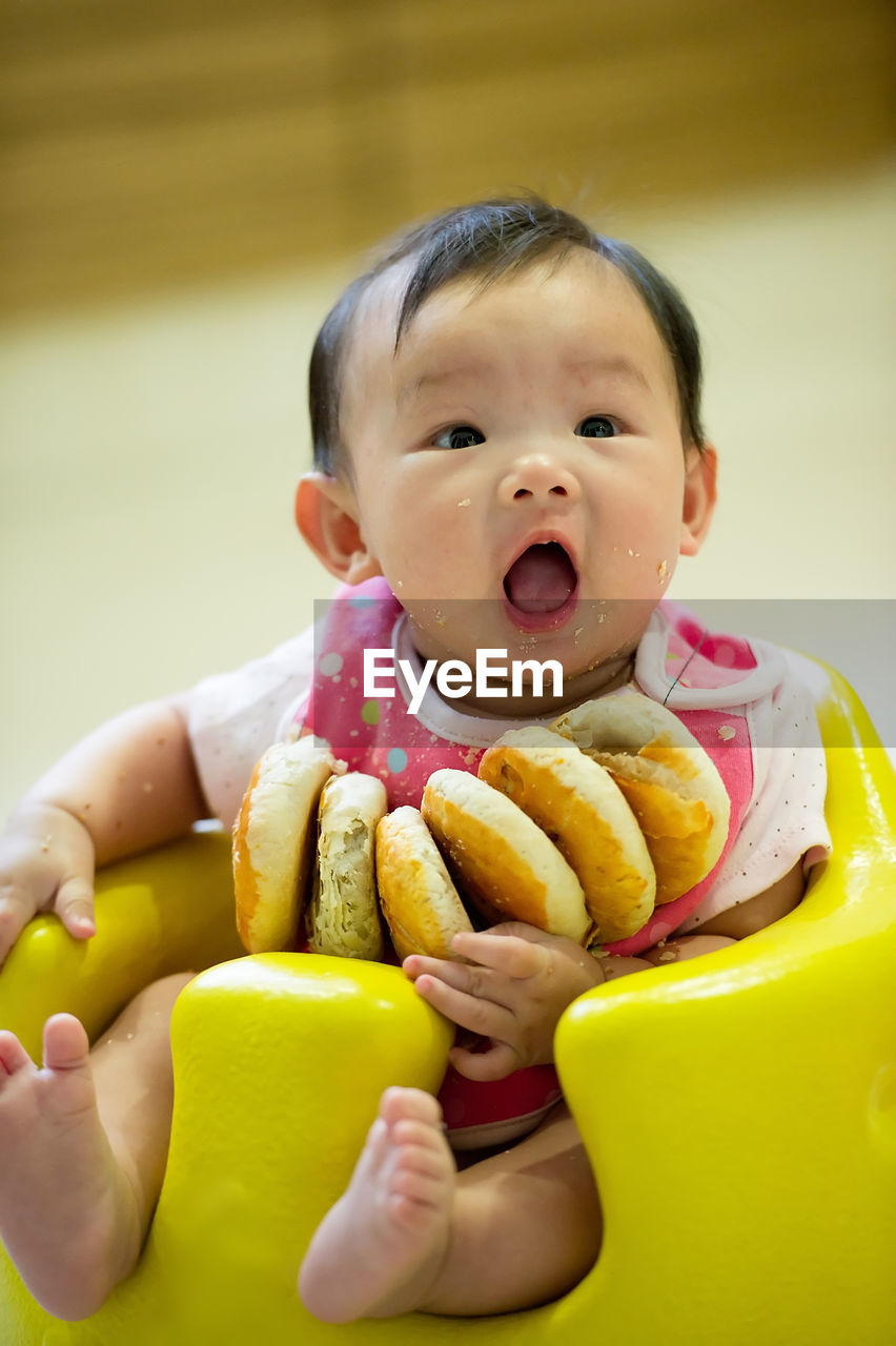 Cute toddler with breads sitting on yellow floor seat at home