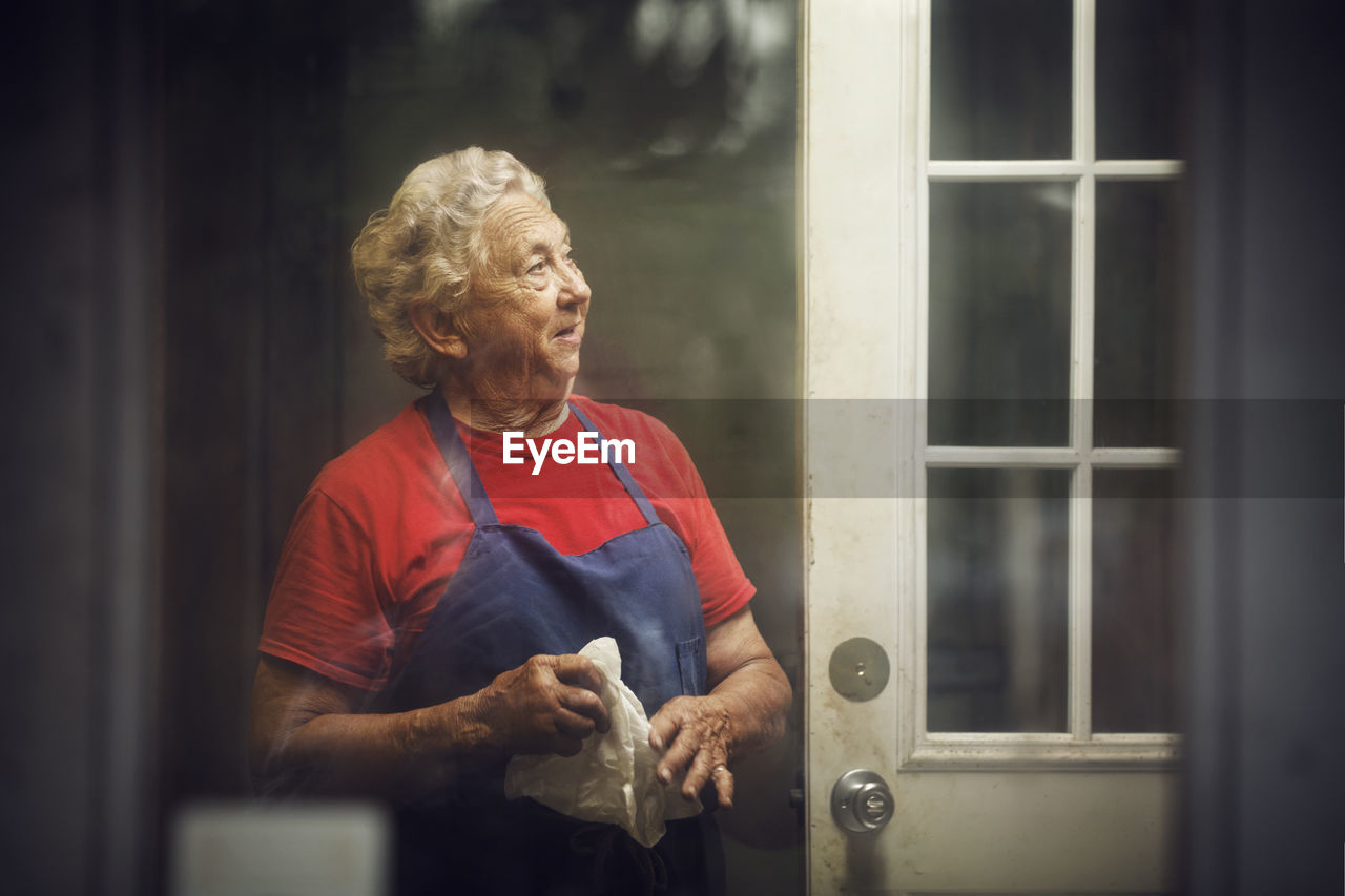 Chef looking away while standing in kitchen seen through glass