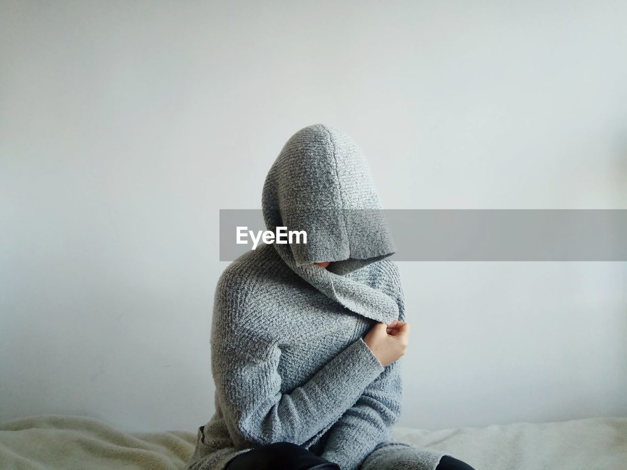 Person wearing warm clothing sitting on bed against wall