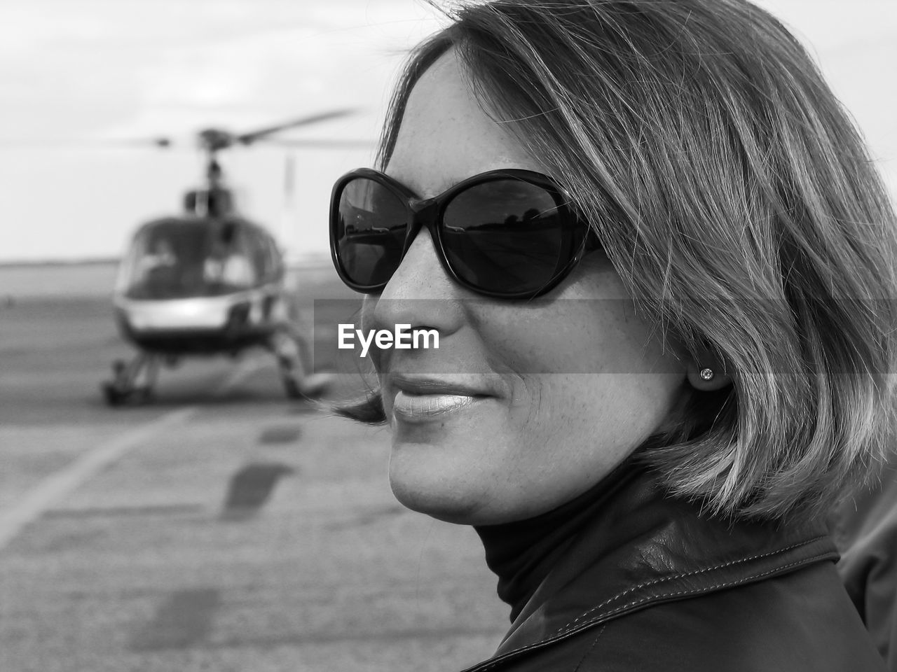Close-up of woman with short hair standing against helicopter in airport runway