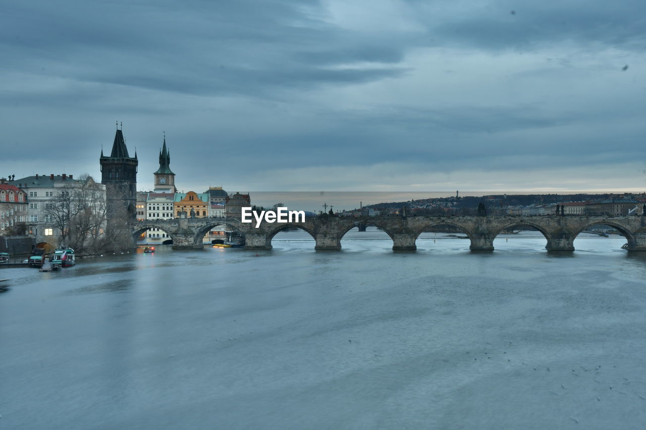 Arch bridge over river against cloudy sky