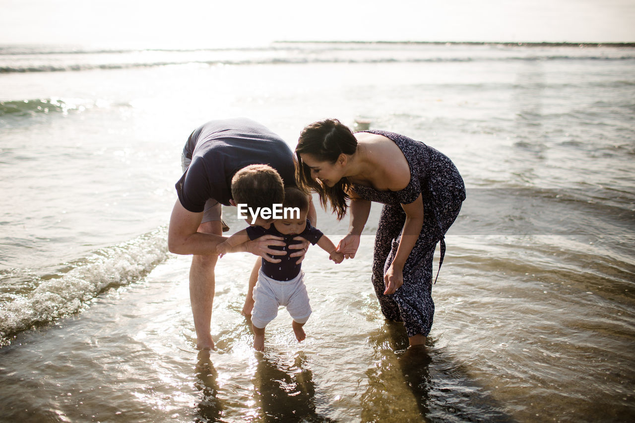 Mid 30's parents playing in ocean with infant son