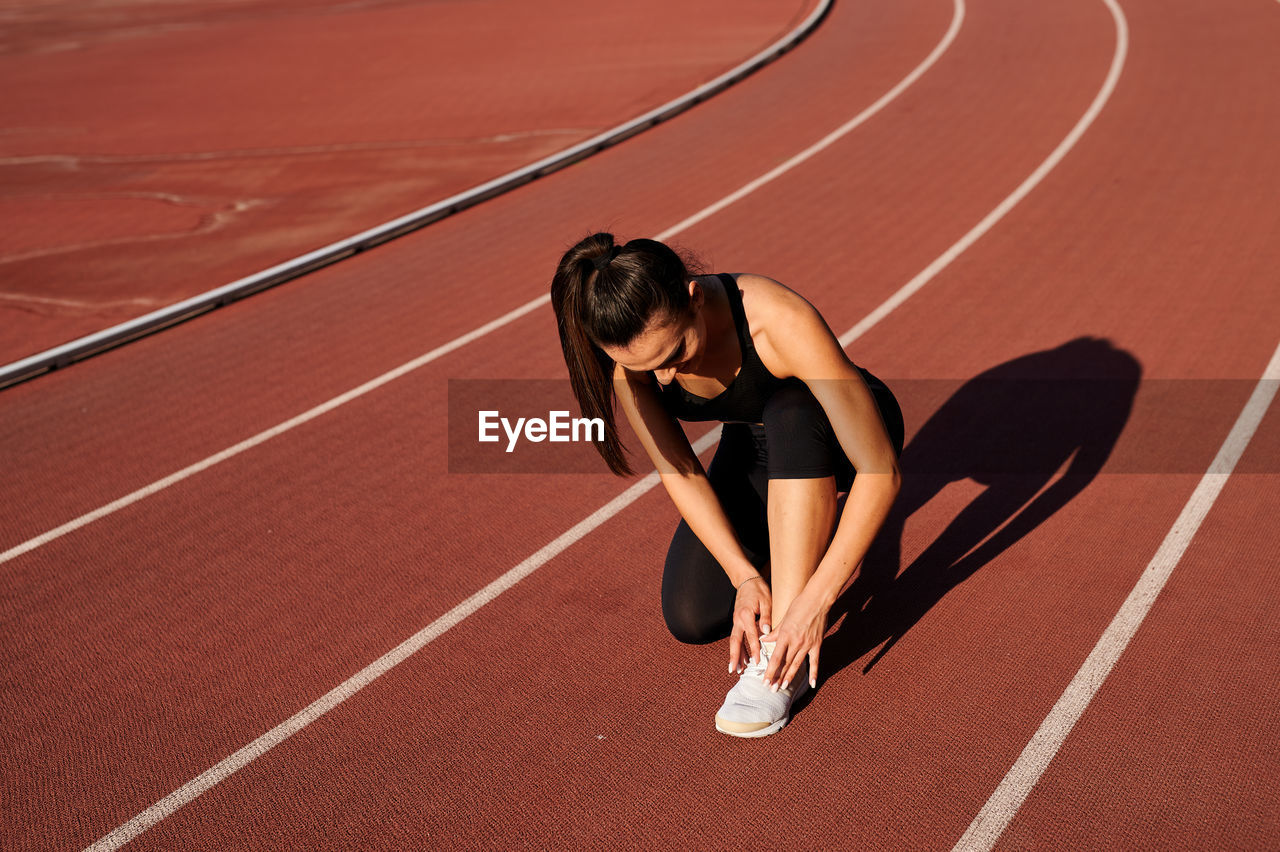 Full length of female athlete tying shoe lace at sports track