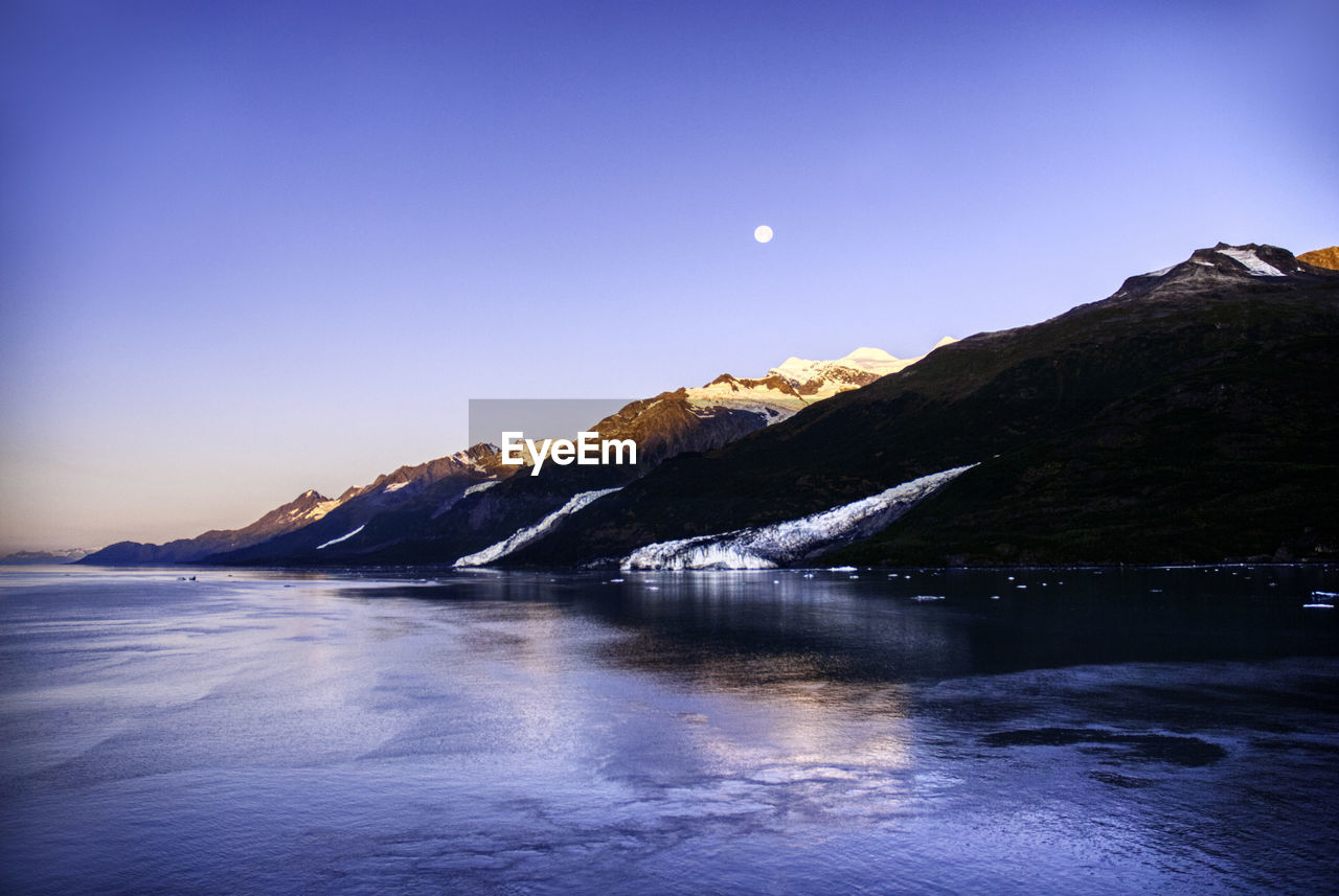 Scenic view of lake and snowcapped mountains against clear blue sky