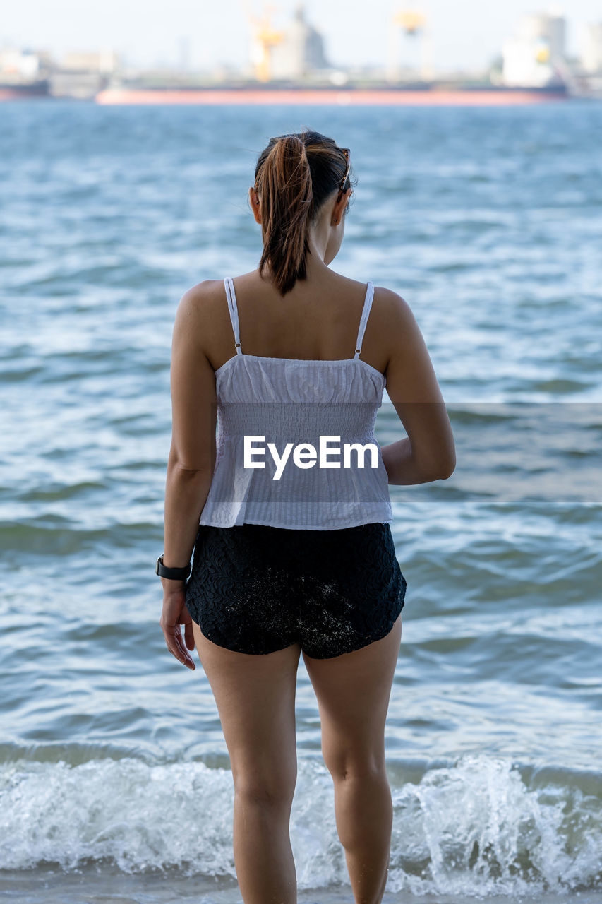 Rear view of woman standing by sea