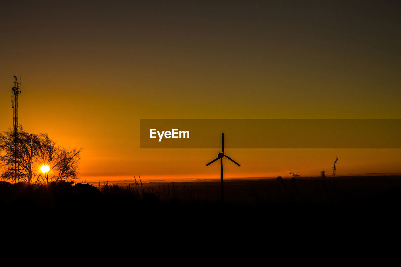 SILHOUETTE OF WIND TURBINES AGAINST ORANGE SKY