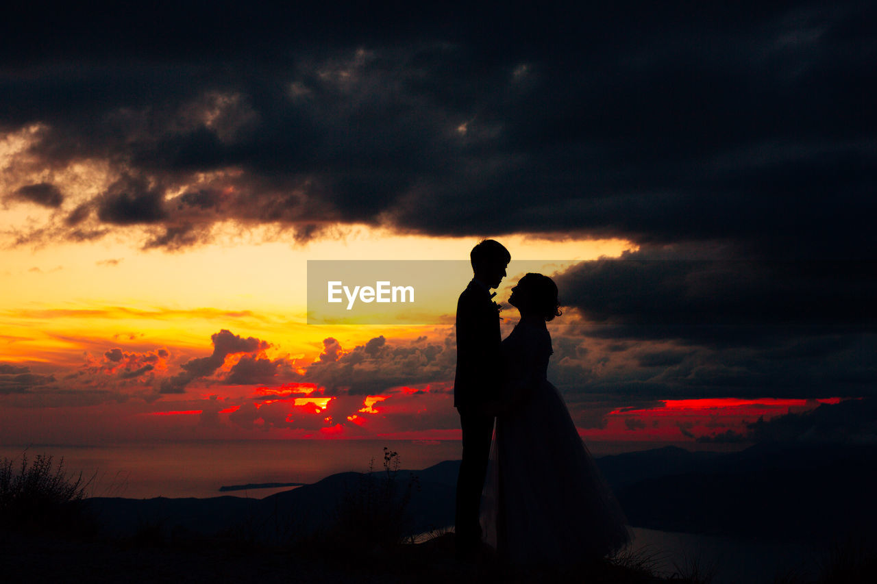 Silhouette couple standing against orange sky