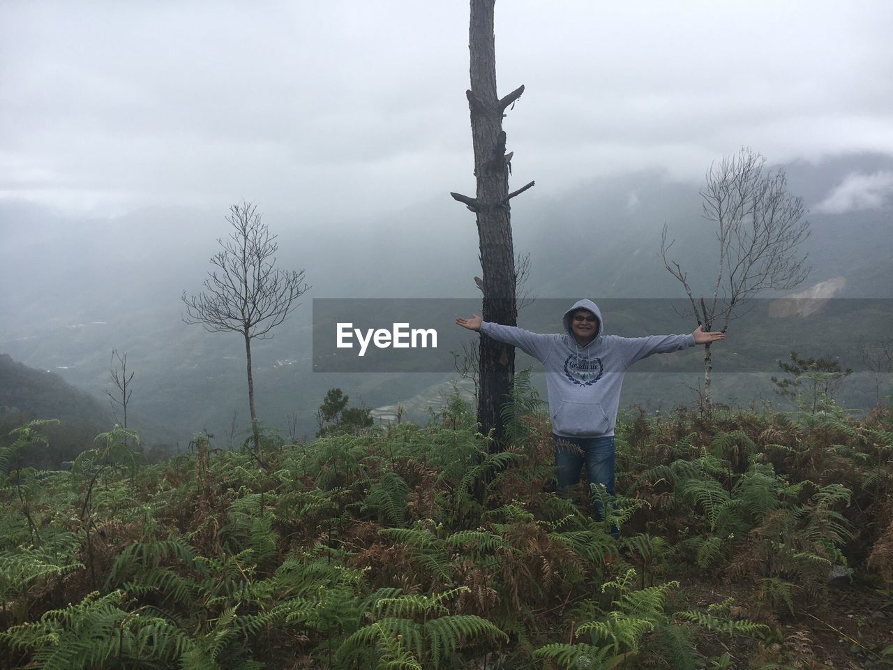 MAN STANDING ON TREE AGAINST SKY