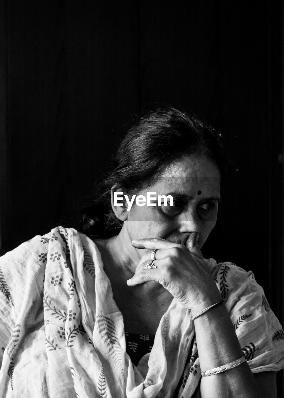 PORTRAIT OF WOMAN LOOKING AWAY WHILE STANDING AGAINST BLACK BACKGROUND