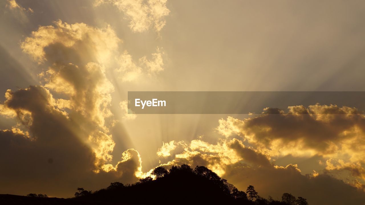 sky, cloud, beauty in nature, sunlight, environment, nature, silhouette, sunset, scenics - nature, dramatic sky, sunbeam, sun, no people, landscape, cloudscape, mountain, outdoors, tranquility, tree, dusk, afterglow, back lit, evening, awe, thunderstorm, storm, horizon, idyllic, tranquil scene