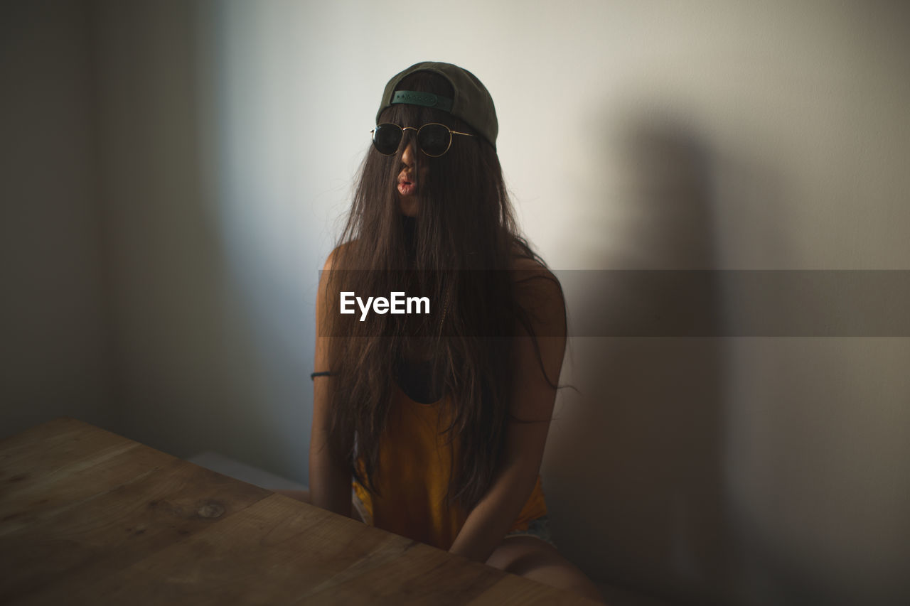 Funny woman with hair covering face puckering lips while sitting by table