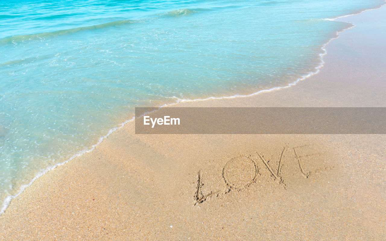 Love word hand writting letter on brown sand beach near small wave of blue water in the sea