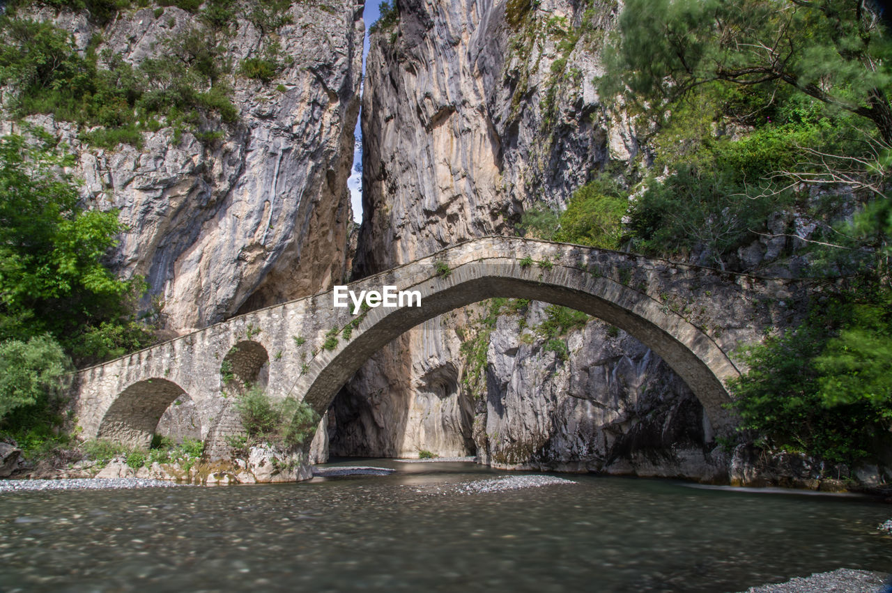 Arch bridge over river amidst trees in greece
