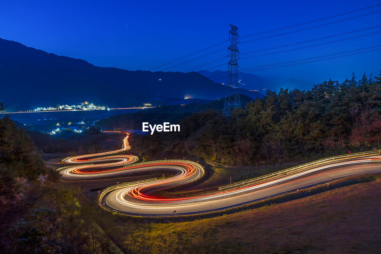 Light trails on road by mountain against sky at night