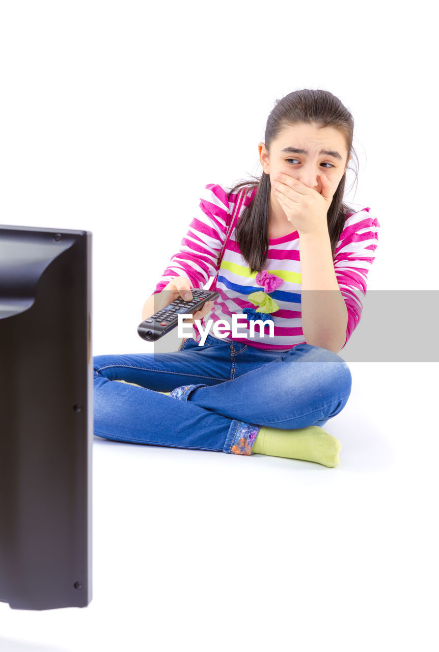 Frightened girl watching television against white background