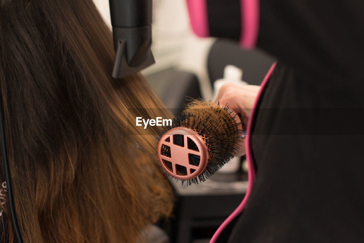 Midsection of hairdresser drying woman hair