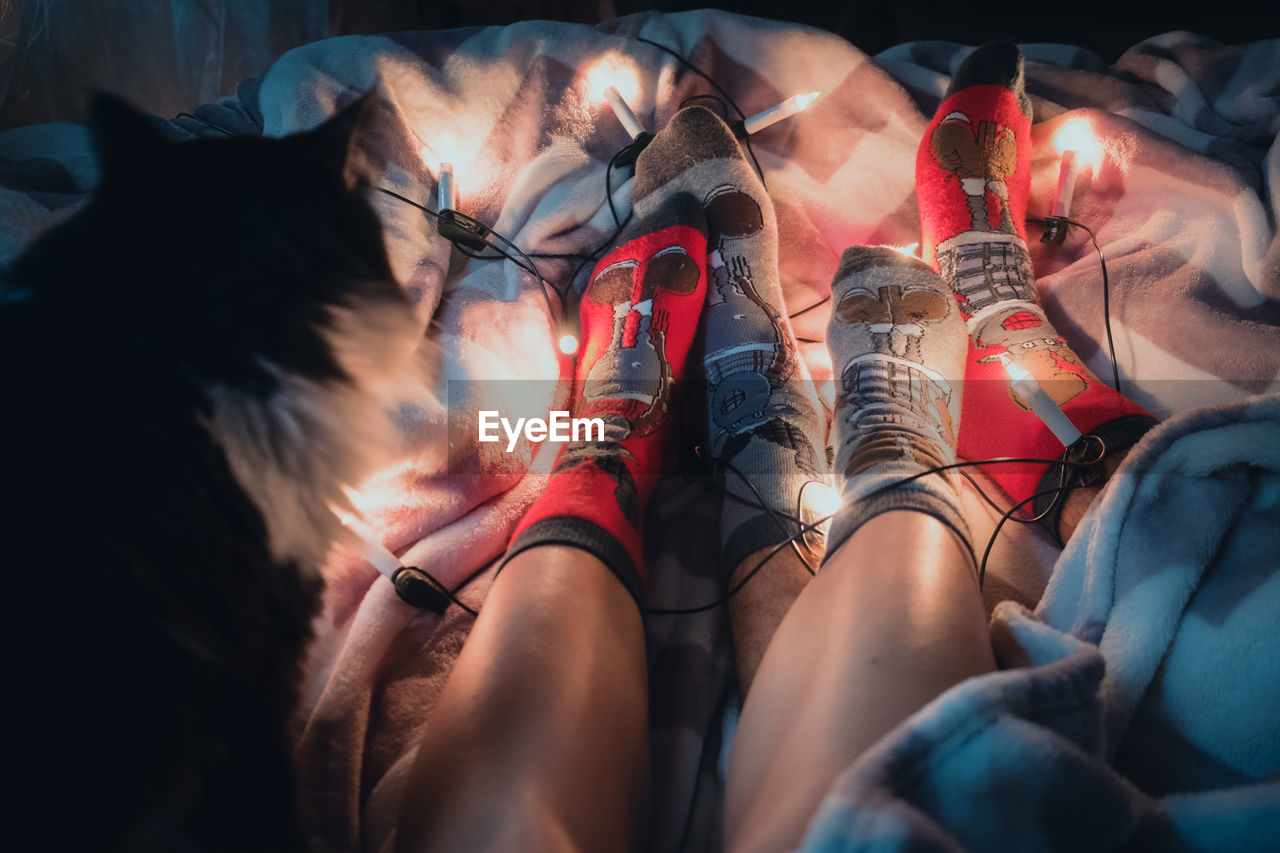 Low section of people wearing socks with illuminated string lights sitting on bed