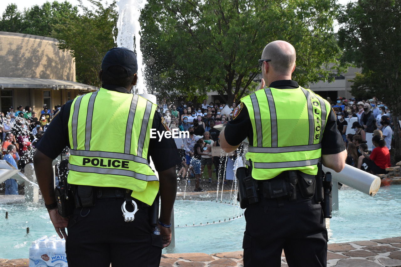 REAR VIEW OF PEOPLE STANDING AGAINST TREES AT RIVERBANK