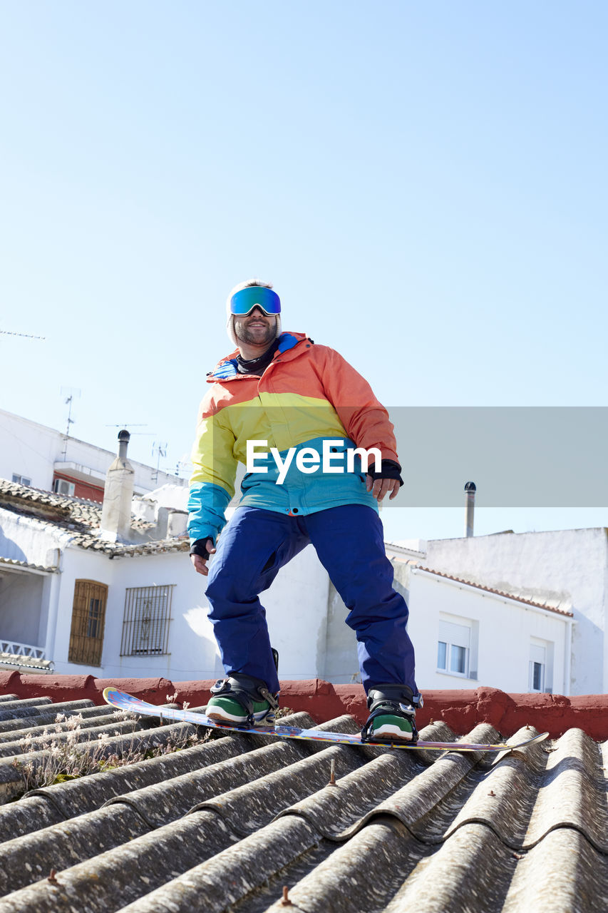 Boy with ski goggles snowboarding on the roof and looking at the camera