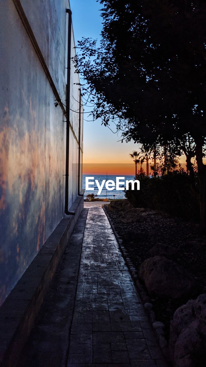 Footpath by sea against sky during sunset