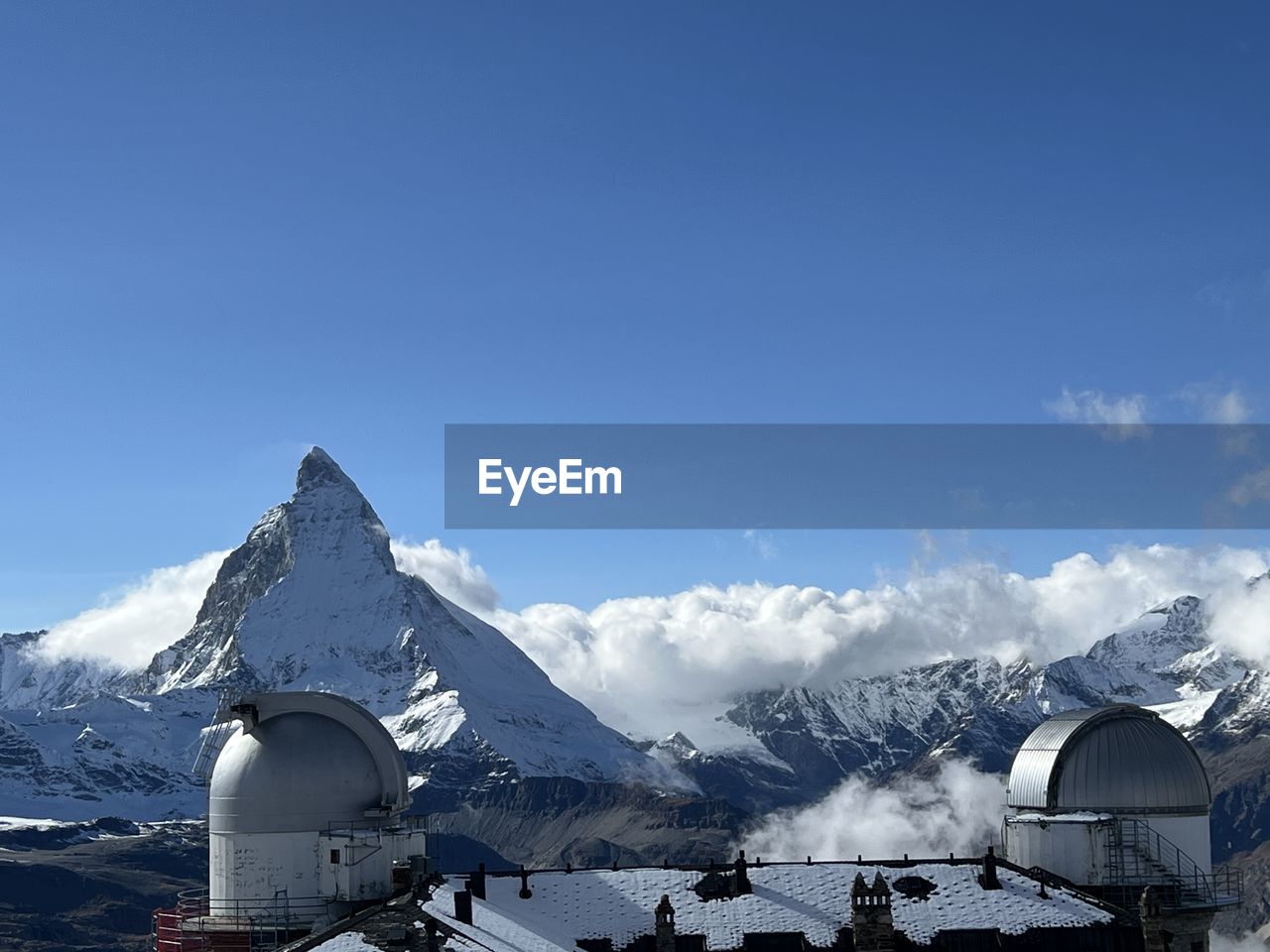 snow, mountain, cold temperature, winter, mountain range, sky, scenics - nature, snowcapped mountain, environment, architecture, landscape, nature, beauty in nature, built structure, travel destinations, building exterior, blue, travel, building, tourism, mountain peak, cloud, no people, day, vacation, hut, holiday, house, frozen, trip, outdoors, resort, tranquil scene, tranquility, winter sports, clear sky, ice, village