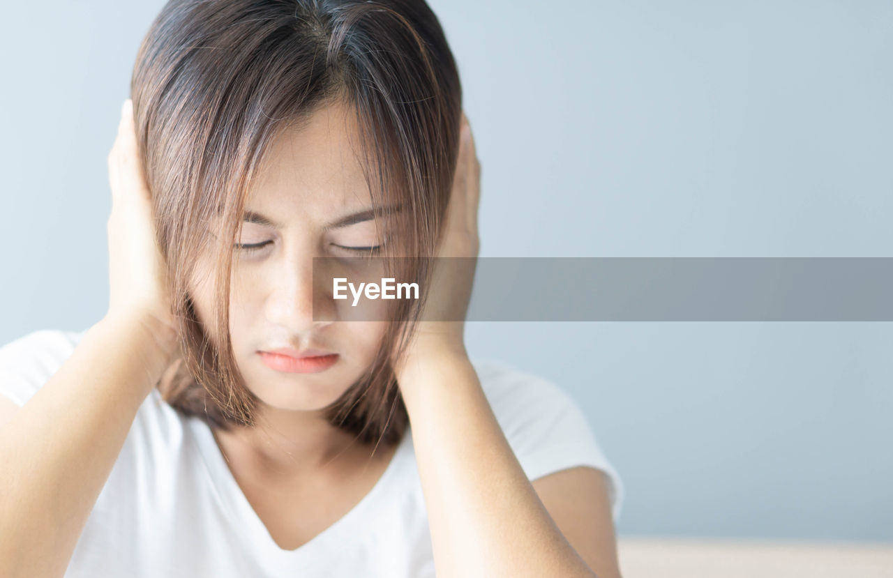 Close-up of stressed woman covering ears against gray wall