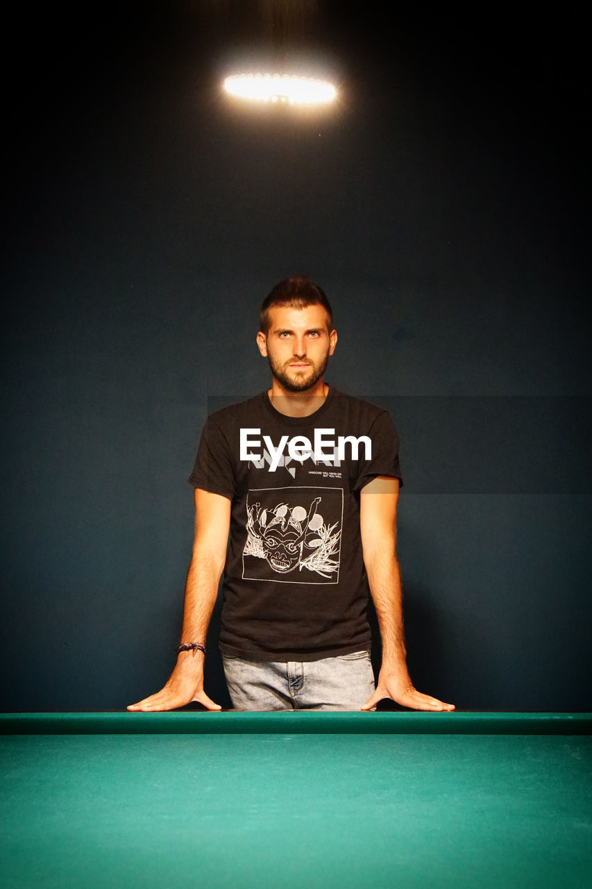 Portrait of young man standing by pool table