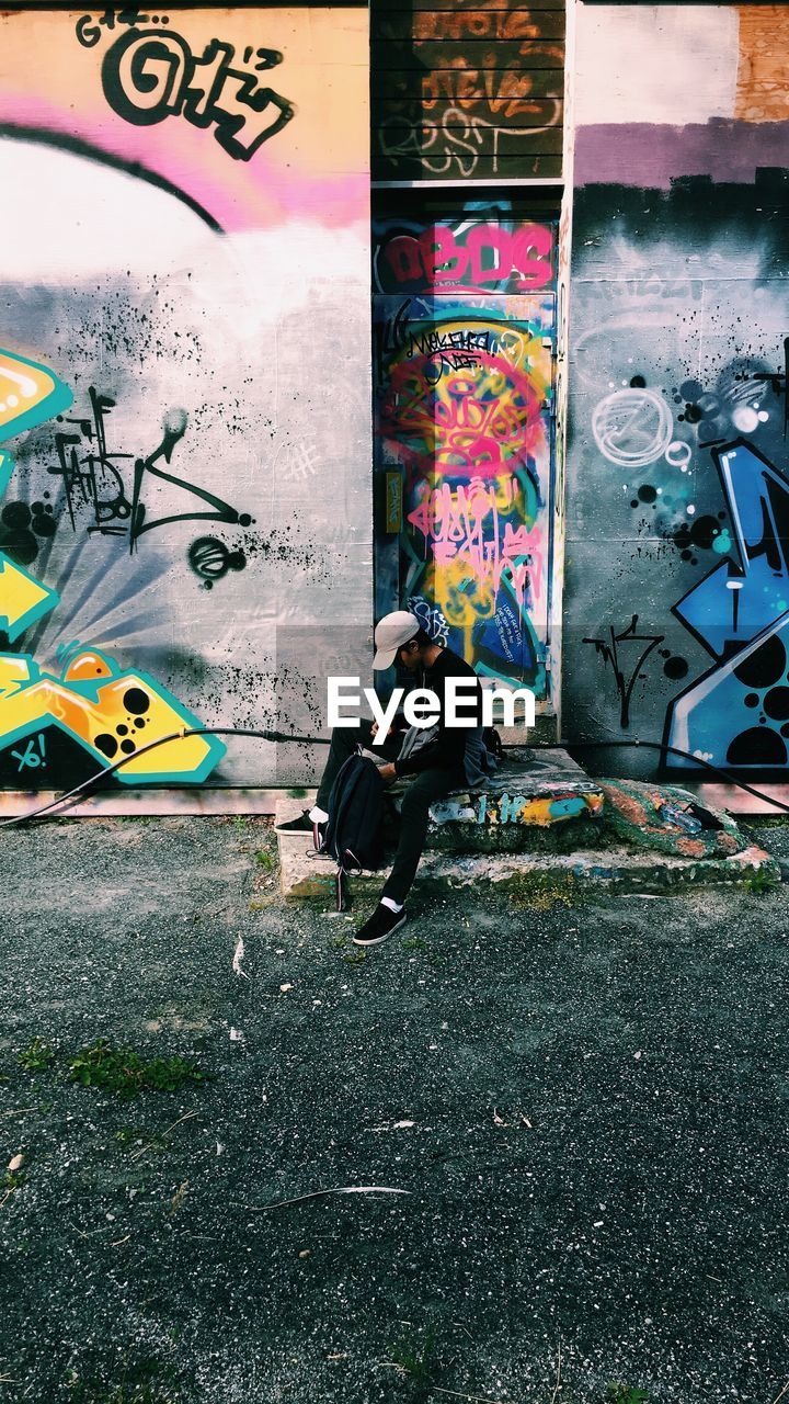 FULL LENGTH OF MAN SITTING AT GRAFFITI