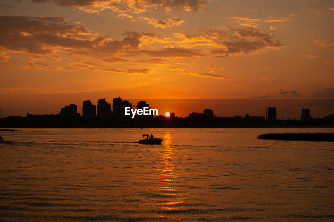 Silhouette buildings by sea against sky during sunset