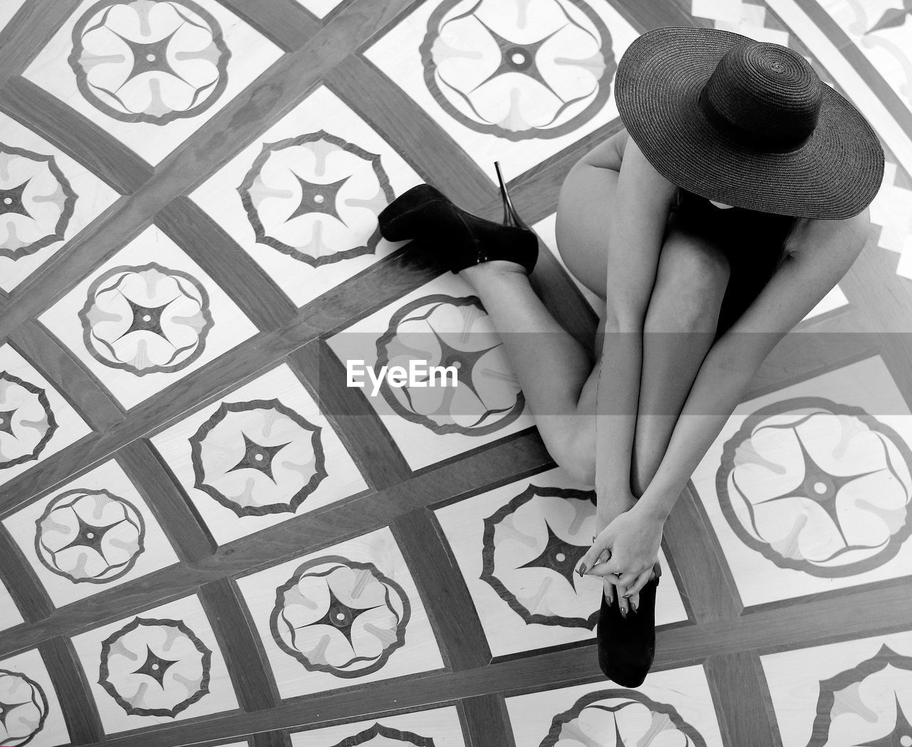 High angle view of naked sensuous woman wearing stilettos and hat sitting on tiled floor