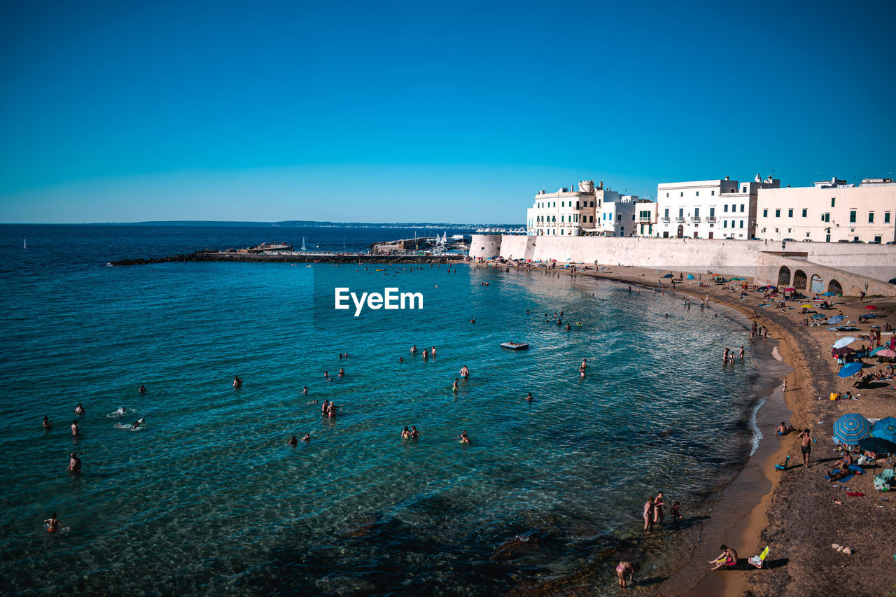 PEOPLE ON BEACH AGAINST CLEAR BLUE SKY IN CITY