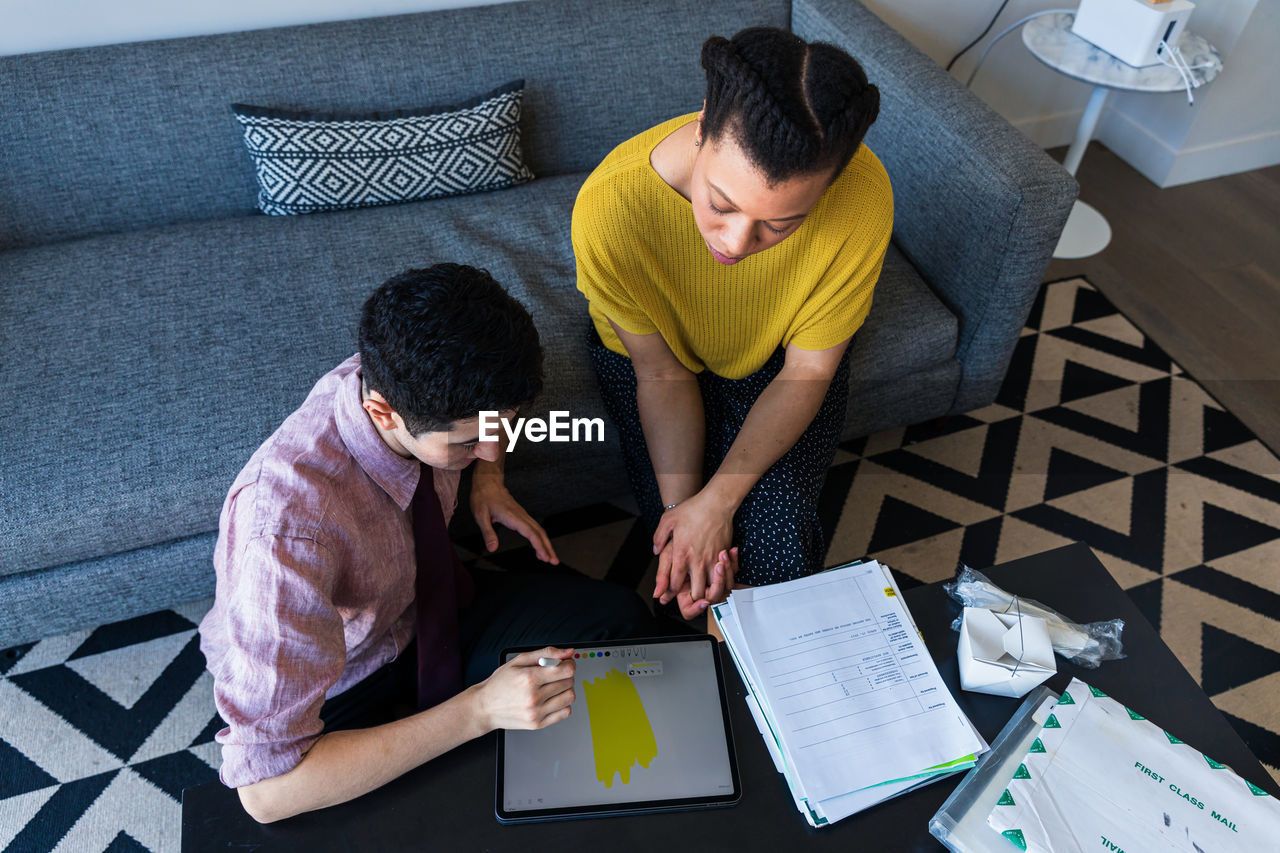 High angle view of male and female colleagues discussing over graphics tablet at table in office