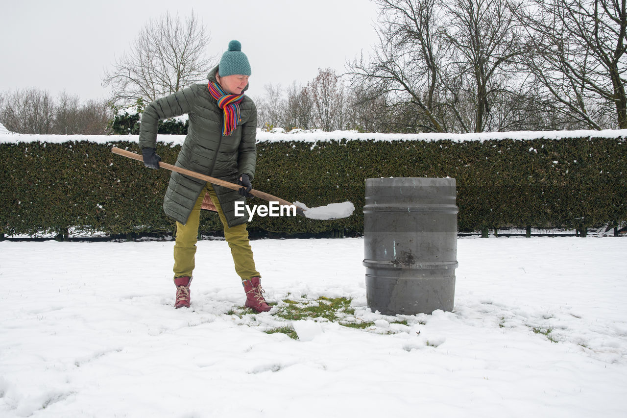 Middle-aged woman is collecting snow in a barrel with a shovel,natural resources