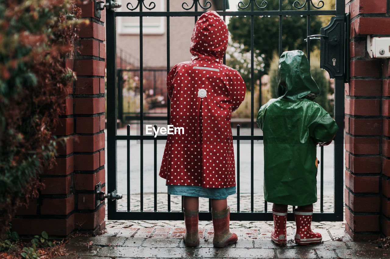 Rear view of children wearing raincoat while standing against gate