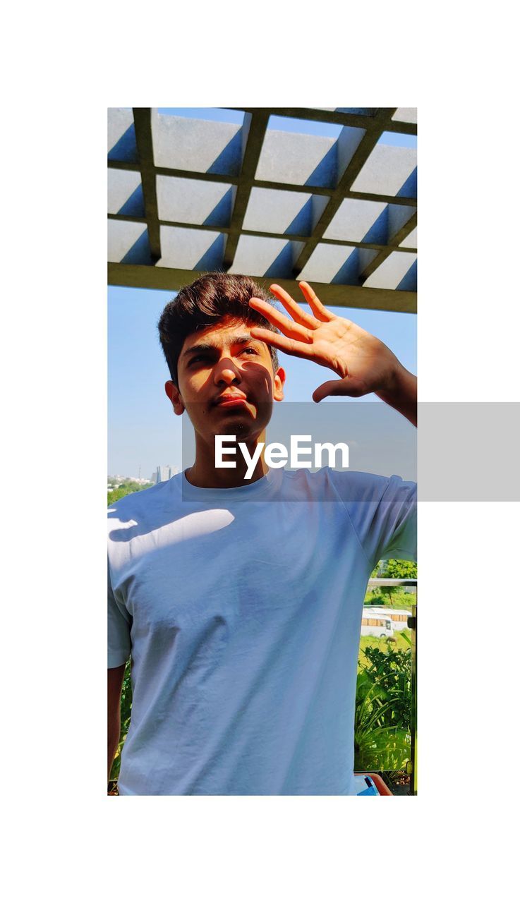 PORTRAIT OF YOUNG MAN STANDING AGAINST SKY