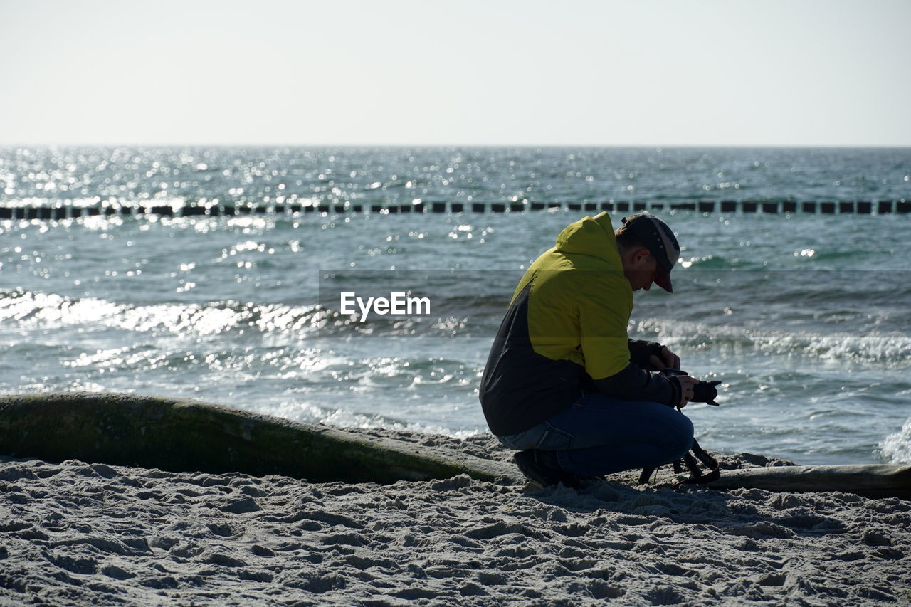 Man crouching while setting up camera at beach