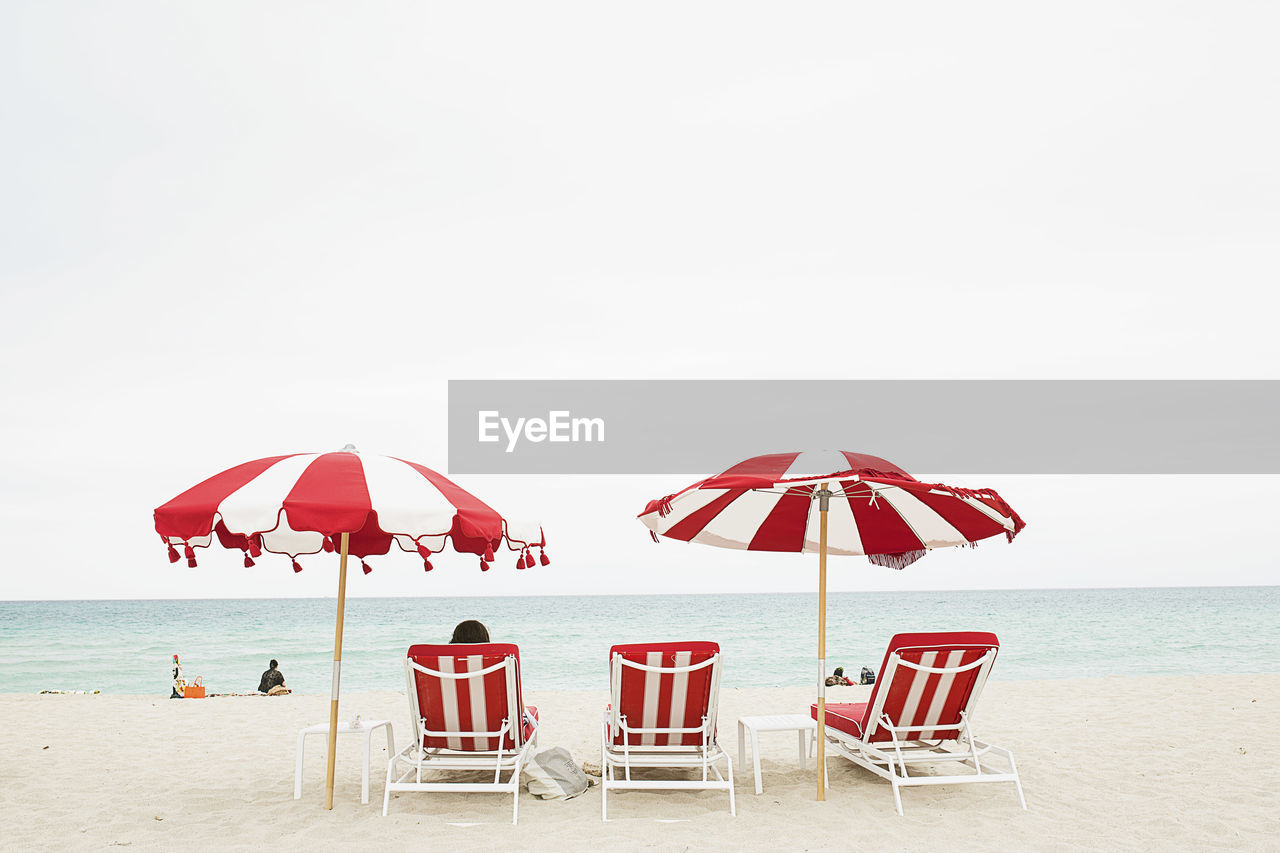 Lounge chairs and parasols at sea shore against clear sky