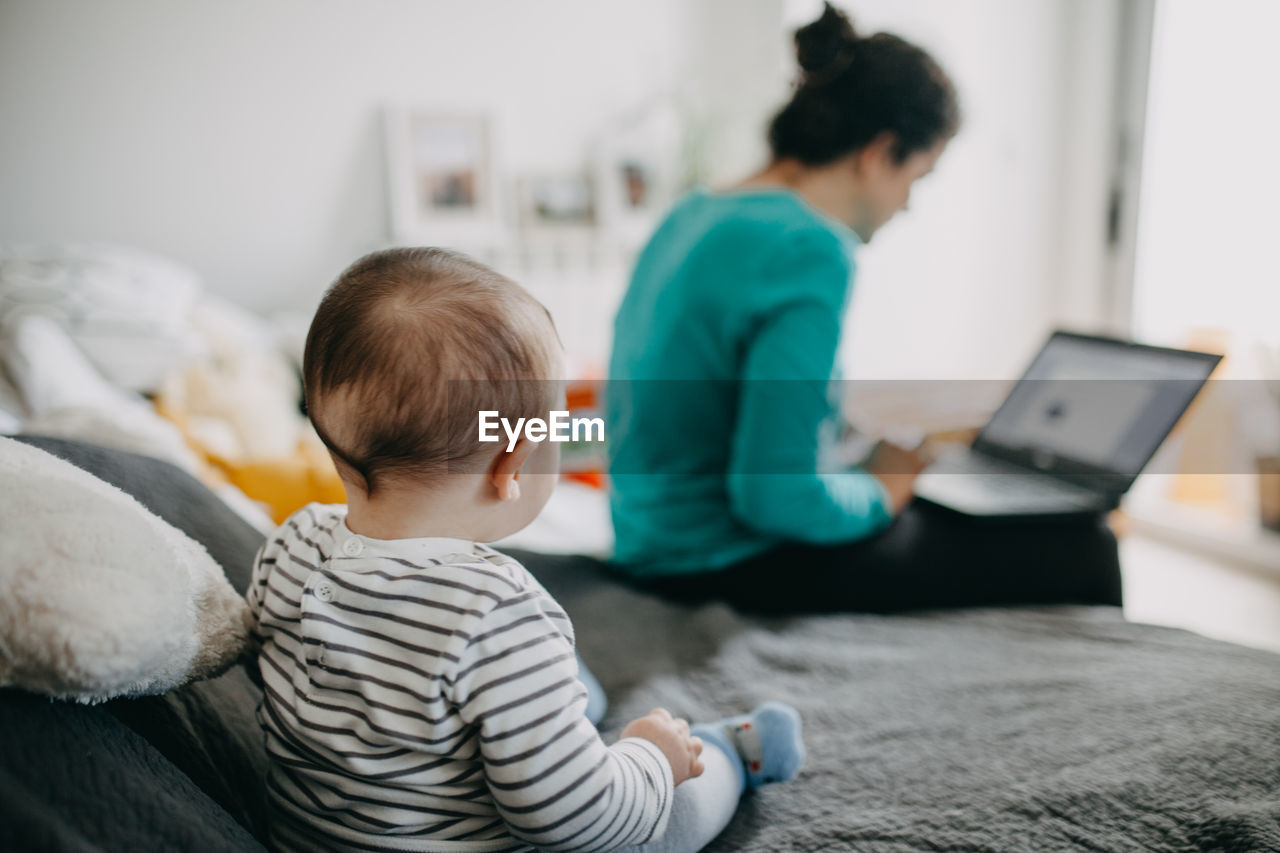 Rear view of baby  watching mother working from home