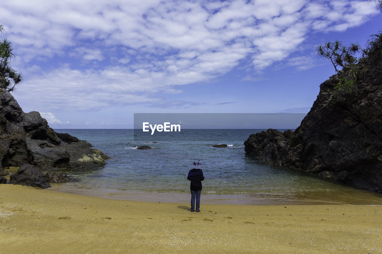 Rear view of woman on rock at beach against sky