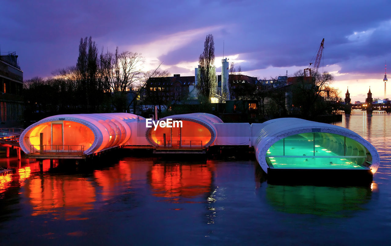 BOATS IN RIVER AGAINST ILLUMINATED CITY AT DUSK